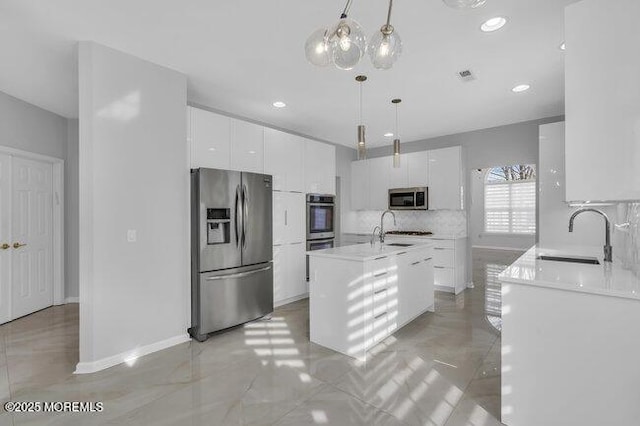 kitchen featuring hanging light fixtures, appliances with stainless steel finishes, sink, white cabinetry, and an island with sink