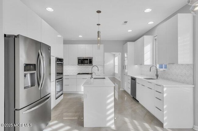 kitchen with appliances with stainless steel finishes, sink, decorative light fixtures, white cabinetry, and a center island with sink