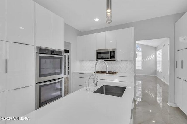 kitchen featuring appliances with stainless steel finishes, white cabinetry, decorative backsplash, sink, and decorative light fixtures