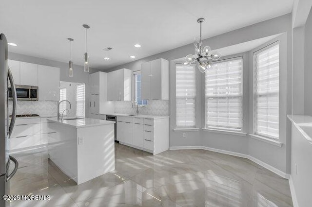 kitchen with white cabinets, decorative light fixtures, stainless steel appliances, tasteful backsplash, and an island with sink