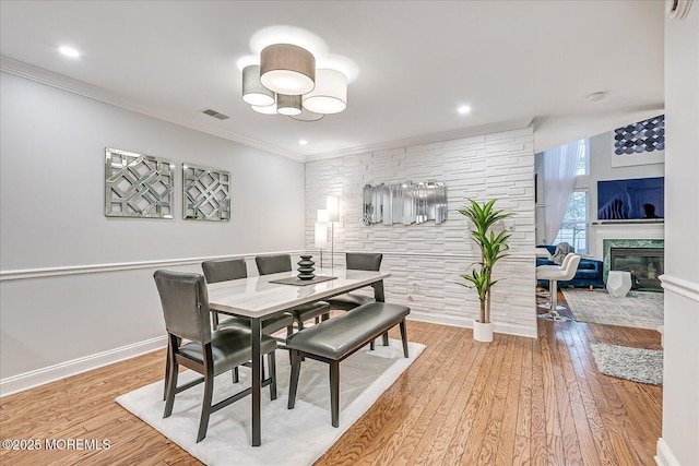 dining space featuring a stone fireplace, ornamental molding, and hardwood / wood-style flooring