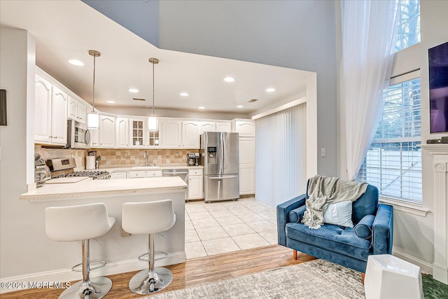 kitchen with kitchen peninsula, stainless steel appliances, sink, white cabinets, and hanging light fixtures