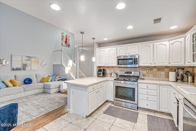 kitchen with pendant lighting, white cabinets, kitchen peninsula, and appliances with stainless steel finishes