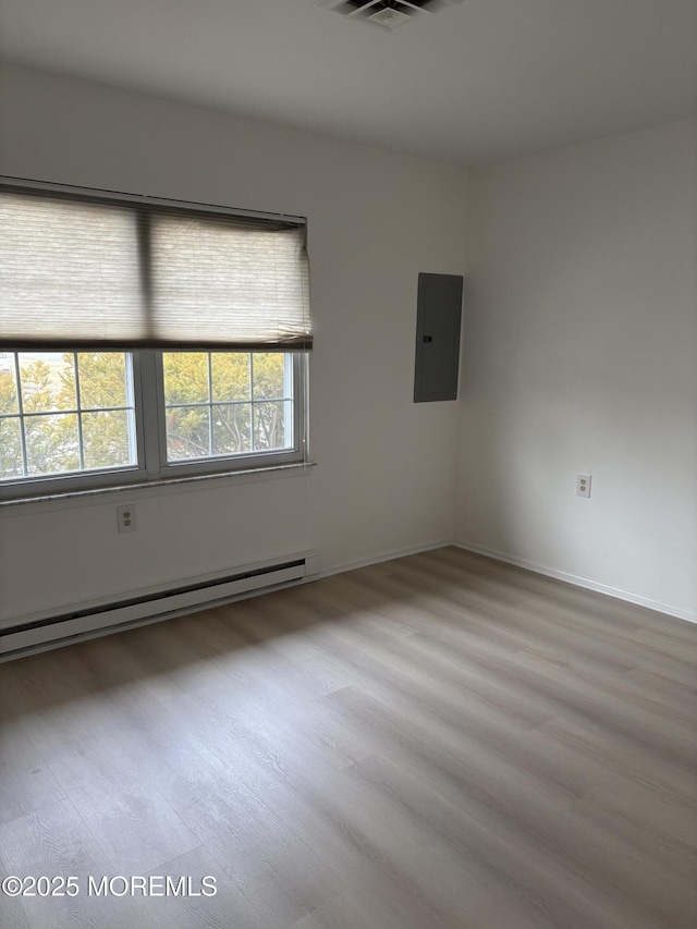 empty room featuring a baseboard radiator, electric panel, and light wood-type flooring