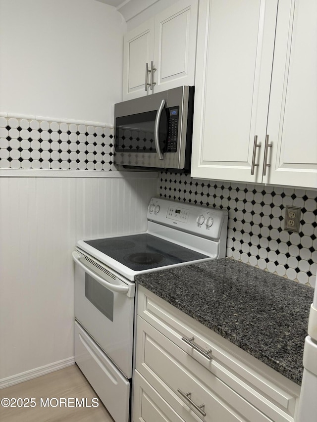 kitchen featuring electric stove, white cabinetry, dark stone countertops, and light wood-type flooring