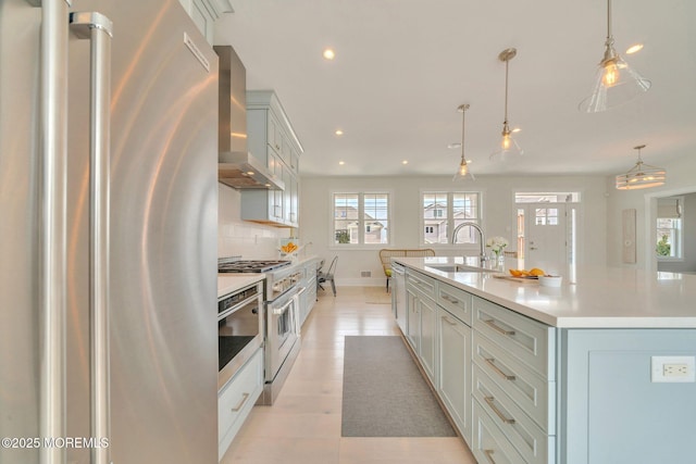 kitchen with wall chimney exhaust hood, stainless steel appliances, sink, pendant lighting, and a center island with sink