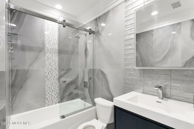 full bathroom featuring vanity, combined bath / shower with glass door, decorative backsplash, toilet, and tile walls