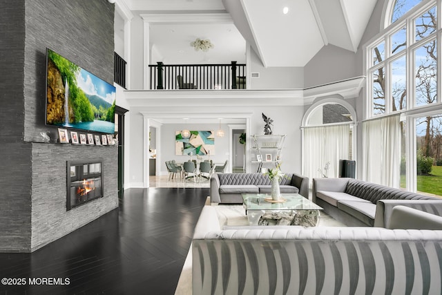 living room featuring dark parquet flooring, a stone fireplace, plenty of natural light, and a high ceiling