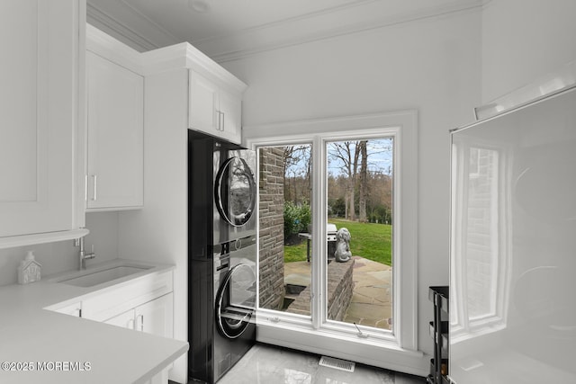 laundry area featuring ornamental molding, stacked washer and dryer, cabinets, and sink