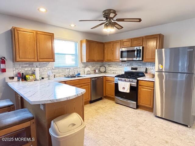 kitchen with sink, ceiling fan, appliances with stainless steel finishes, a kitchen bar, and kitchen peninsula