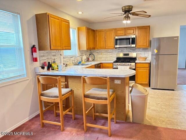 kitchen with kitchen peninsula, decorative backsplash, sink, and appliances with stainless steel finishes