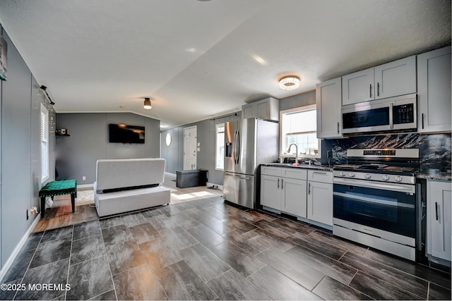 kitchen with backsplash, stainless steel appliances, vaulted ceiling, sink, and a barn door