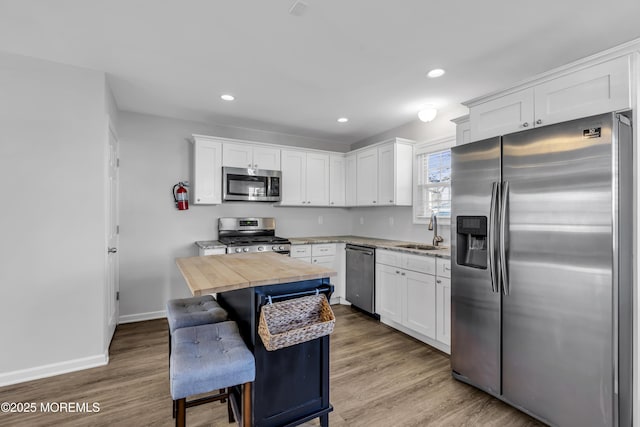 kitchen featuring a kitchen bar, appliances with stainless steel finishes, sink, white cabinets, and light hardwood / wood-style floors