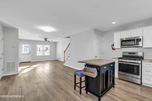 kitchen with white cabinets, a kitchen breakfast bar, butcher block countertops, and appliances with stainless steel finishes