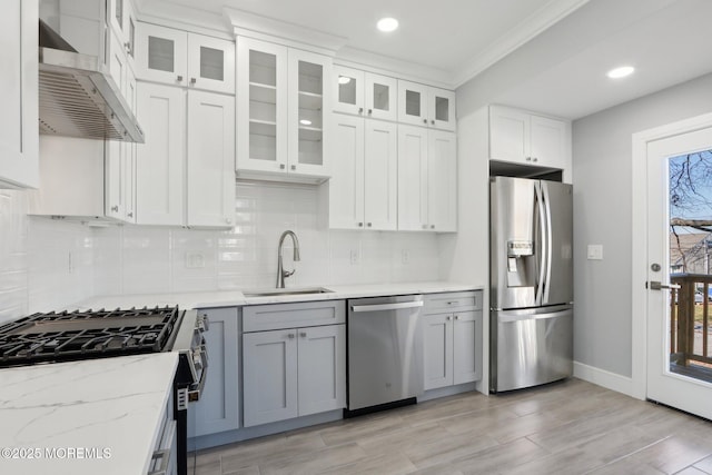 kitchen with stainless steel appliances, light stone counters, wall chimney exhaust hood, white cabinets, and sink