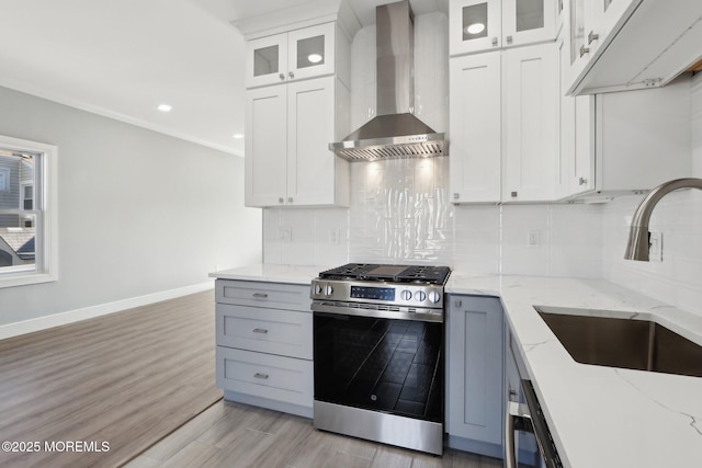 kitchen with gas stove, wall chimney range hood, sink, and white cabinetry