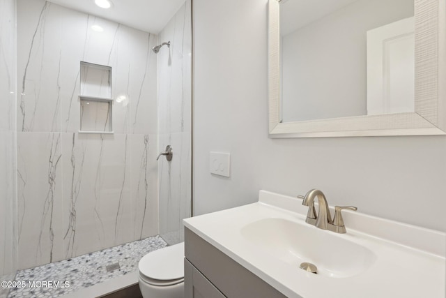 bathroom featuring toilet, vanity, and tiled shower