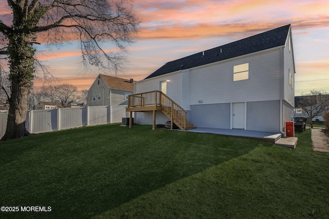 back house at dusk featuring a lawn, central AC, and a patio