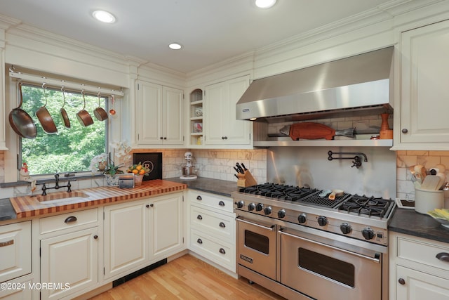 kitchen featuring wooden counters, high end stove, wall chimney exhaust hood, and backsplash