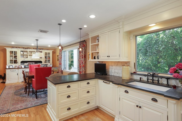 kitchen featuring pendant lighting, crown molding, sink, light hardwood / wood-style flooring, and kitchen peninsula