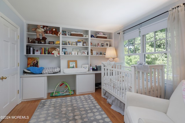 bedroom featuring light hardwood / wood-style floors, crown molding, and a nursery area