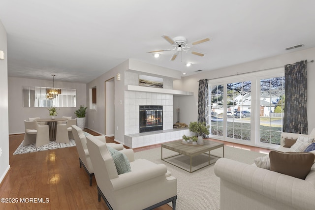 living room with a fireplace, wood-type flooring, and ceiling fan with notable chandelier