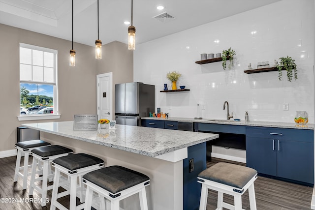 kitchen with sink, decorative backsplash, blue cabinetry, a kitchen bar, and stainless steel refrigerator