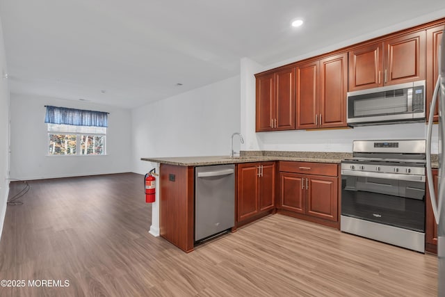 kitchen featuring sink, light hardwood / wood-style flooring, light stone counters, kitchen peninsula, and stainless steel appliances