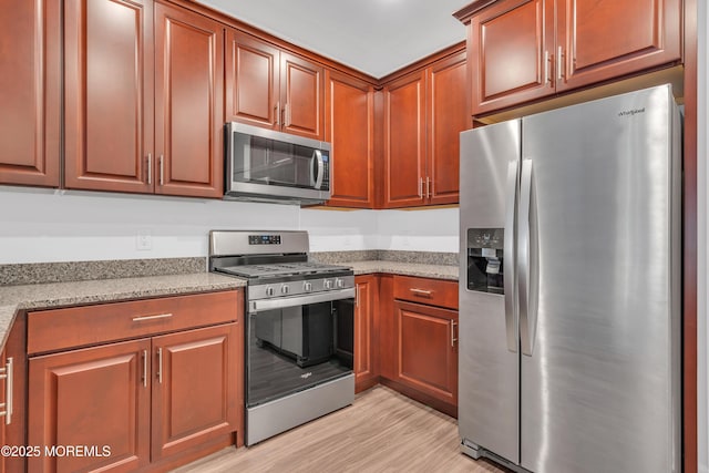 kitchen with light stone countertops, stainless steel appliances, and light wood-type flooring