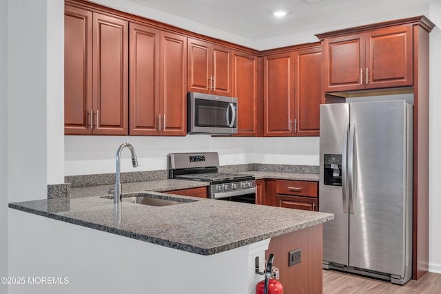 kitchen featuring kitchen peninsula, stainless steel appliances, dark stone countertops, and sink