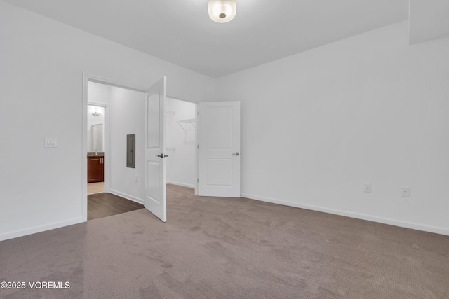 unfurnished bedroom with electric panel, a walk in closet, a closet, and dark colored carpet