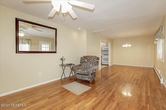 living area featuring ceiling fan with notable chandelier, light wood-type flooring, and a baseboard radiator