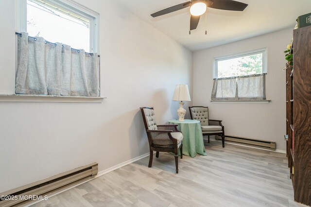 living area featuring ceiling fan, light hardwood / wood-style flooring, and a baseboard heating unit