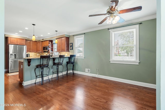 kitchen featuring a breakfast bar area, ornamental molding, appliances with stainless steel finishes, kitchen peninsula, and backsplash