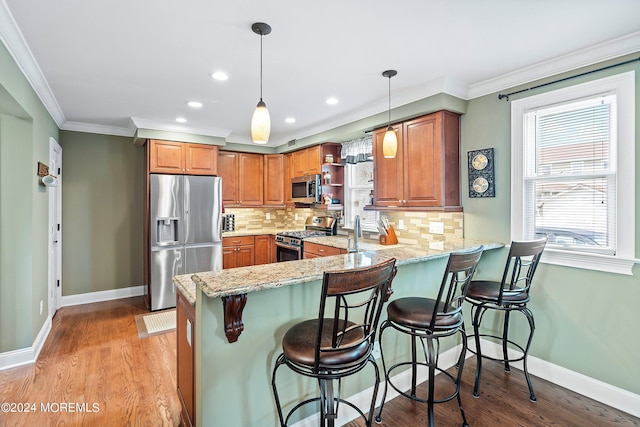 kitchen with appliances with stainless steel finishes, pendant lighting, tasteful backsplash, kitchen peninsula, and light stone countertops