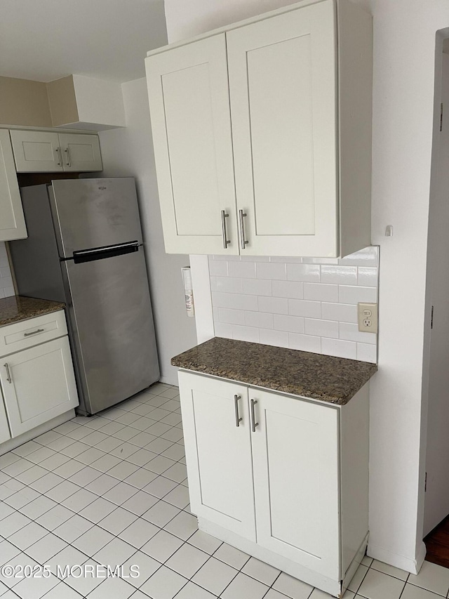 kitchen with stainless steel refrigerator, white cabinets, light tile patterned flooring, decorative backsplash, and dark stone counters