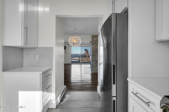 kitchen with backsplash, baseboard heating, a notable chandelier, white cabinetry, and stainless steel refrigerator