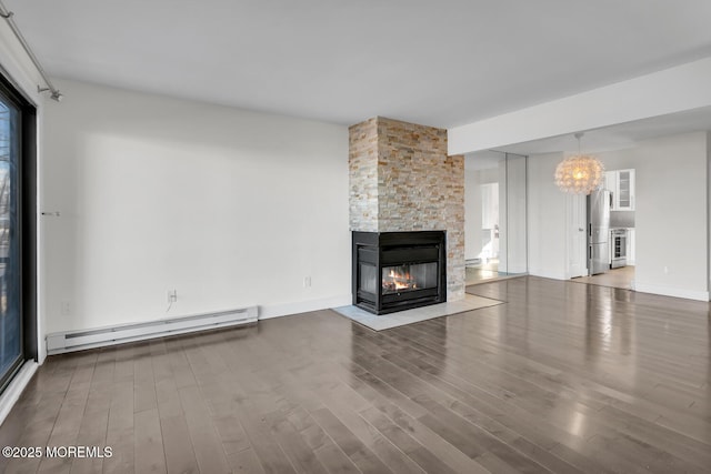 unfurnished living room with a fireplace, wood-type flooring, an inviting chandelier, and a baseboard heating unit