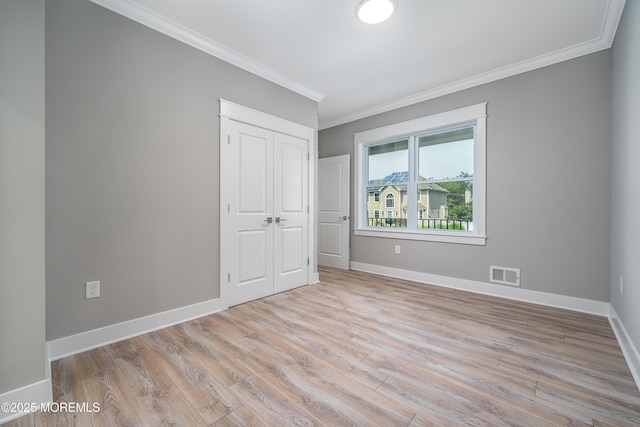 unfurnished bedroom with light wood-type flooring, crown molding, and a closet