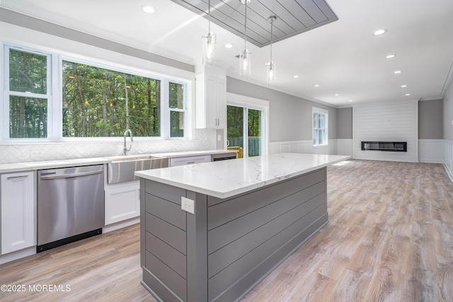 kitchen with light stone countertops, white cabinetry, sink, stainless steel dishwasher, and a kitchen island