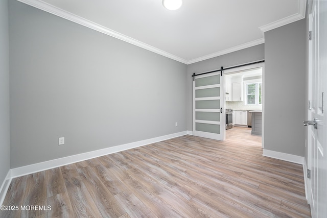 unfurnished room with a barn door, ornamental molding, light wood-style flooring, and baseboards