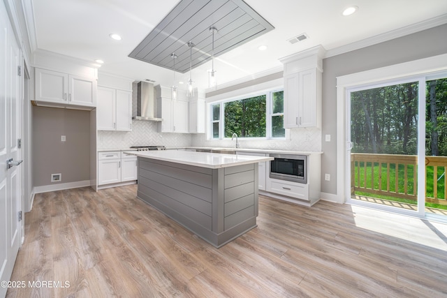 kitchen with appliances with stainless steel finishes, wall chimney range hood, pendant lighting, white cabinets, and a kitchen island