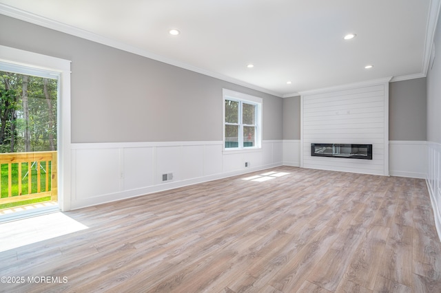 unfurnished living room with visible vents, a wainscoted wall, light wood-style flooring, ornamental molding, and a fireplace