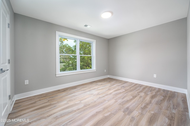 spare room featuring light wood-type flooring, visible vents, and baseboards