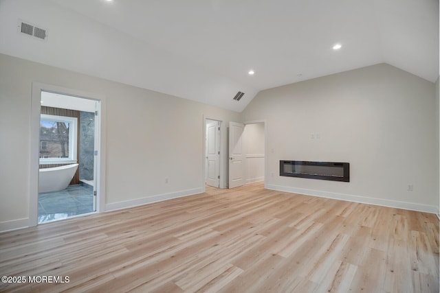 unfurnished living room featuring light wood-style floors, visible vents, vaulted ceiling, and a glass covered fireplace