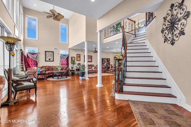 foyer entrance with hardwood / wood-style flooring, ceiling fan, ornate columns, and a high ceiling