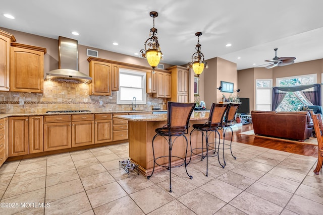 kitchen with light stone countertops, pendant lighting, a center island, and wall chimney range hood