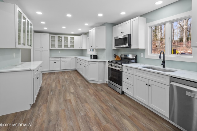 kitchen with light stone countertops, appliances with stainless steel finishes, sink, hardwood / wood-style flooring, and white cabinets