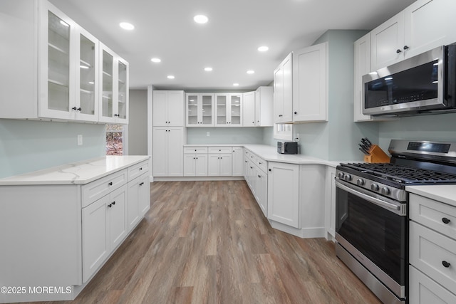 kitchen featuring white cabinets, appliances with stainless steel finishes, light wood-type flooring, and light stone countertops