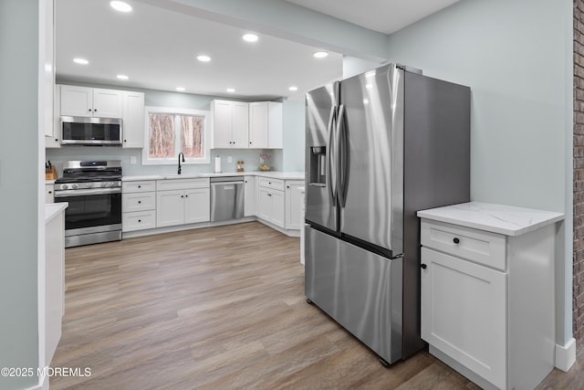 kitchen with sink, light stone countertops, light wood-type flooring, appliances with stainless steel finishes, and white cabinetry